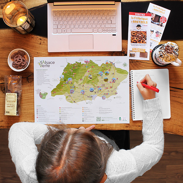 Photo d'une femme qui prépare ses sorties en Alsace, avec un ordinateur, des prospectus, dont la Fabrique à Bretzels